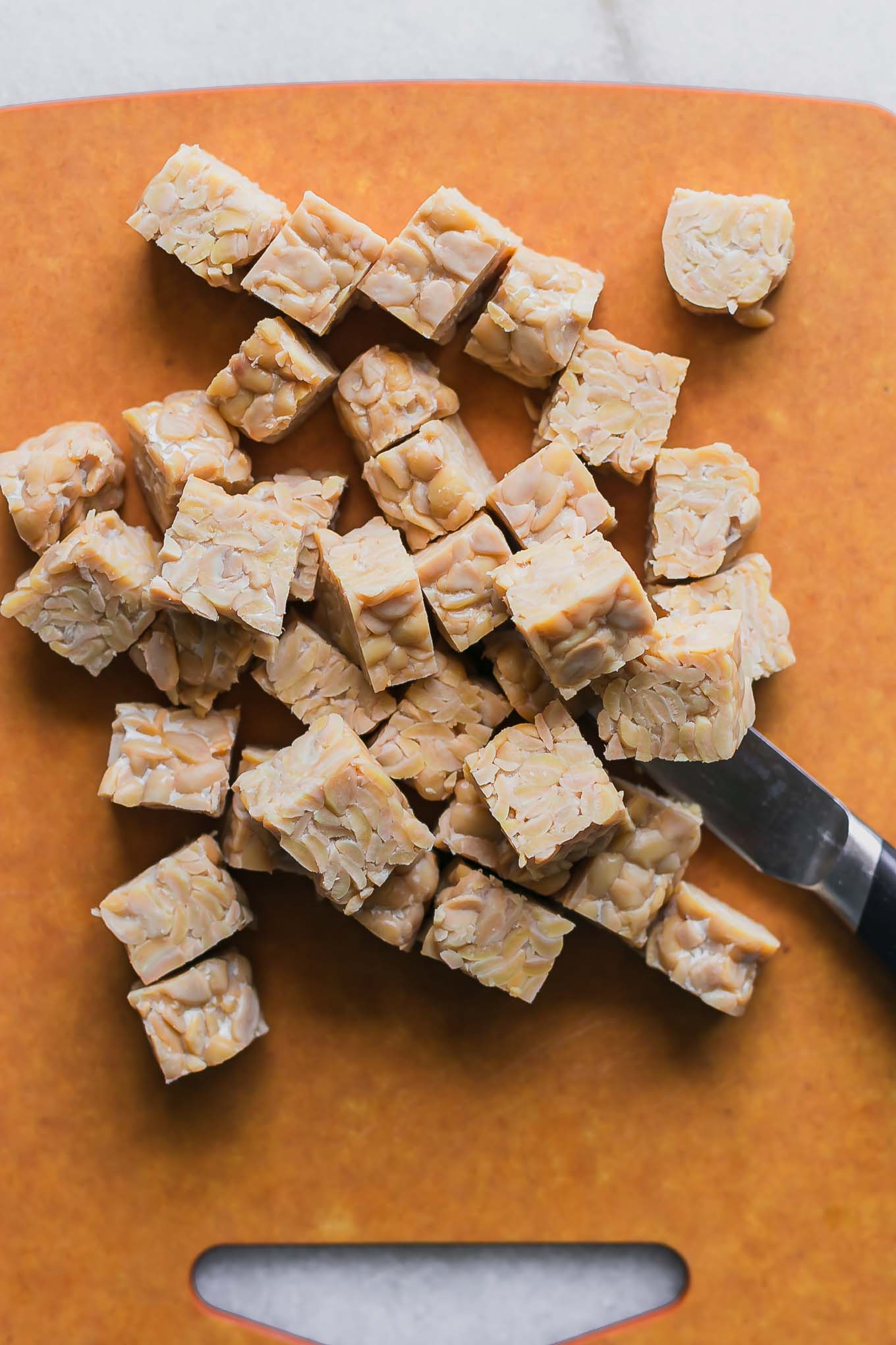 tempeh cut into cubes on a wood cutting board with a knife