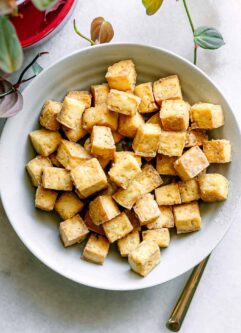 a bowl with crispy tofu on a white table with a gold fork