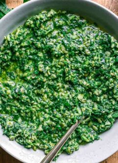 a bowl of dandelion leaves pesto sauce on a wood table with fresh dandelion greens