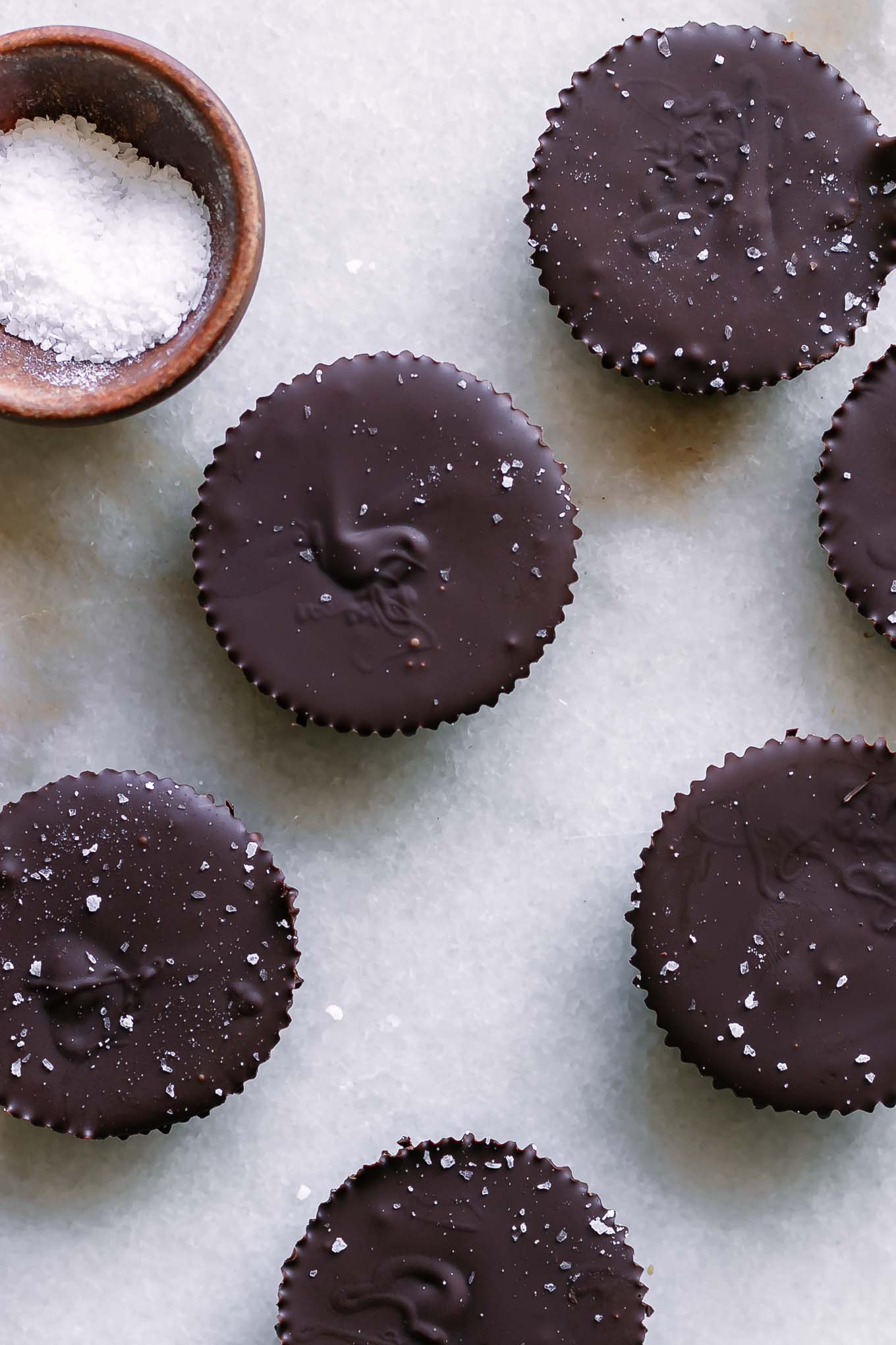 chocolate peanut butter cups on a white table with a bowl of sea salt