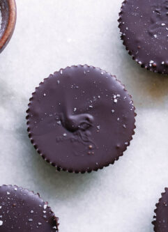 dark chocolate peanut butter cups on a white table with a bowl of sea salt for garnish