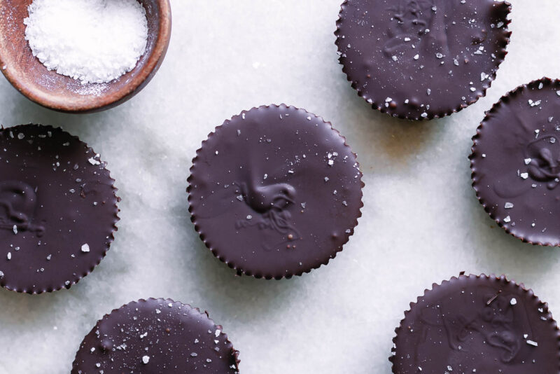 dark chocolate peanut butter cups on a white table with a bowl of sea salt for garnish