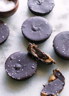 homemade chocolate peanut butter cups on a white table with one cut in half with peanut butter coming out