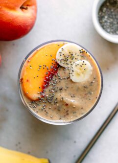 a smoothie garnished with a peach slice and banana slices on a white table