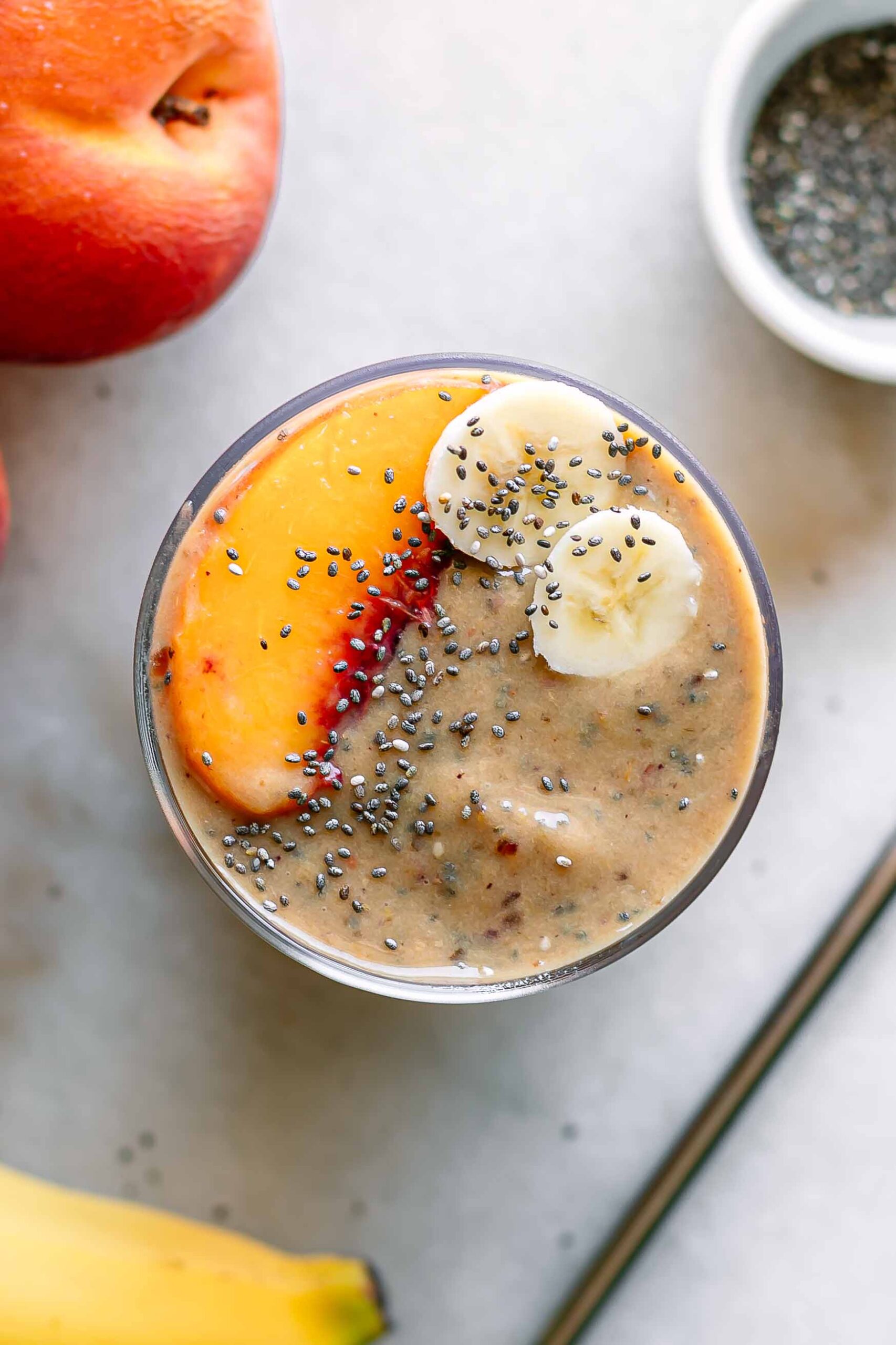 a smoothie garnished with a peach slice and banana slices on a white table