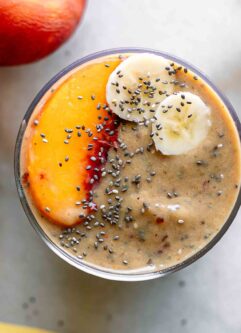the top of a smoothie with peach and banana slices on a white table
