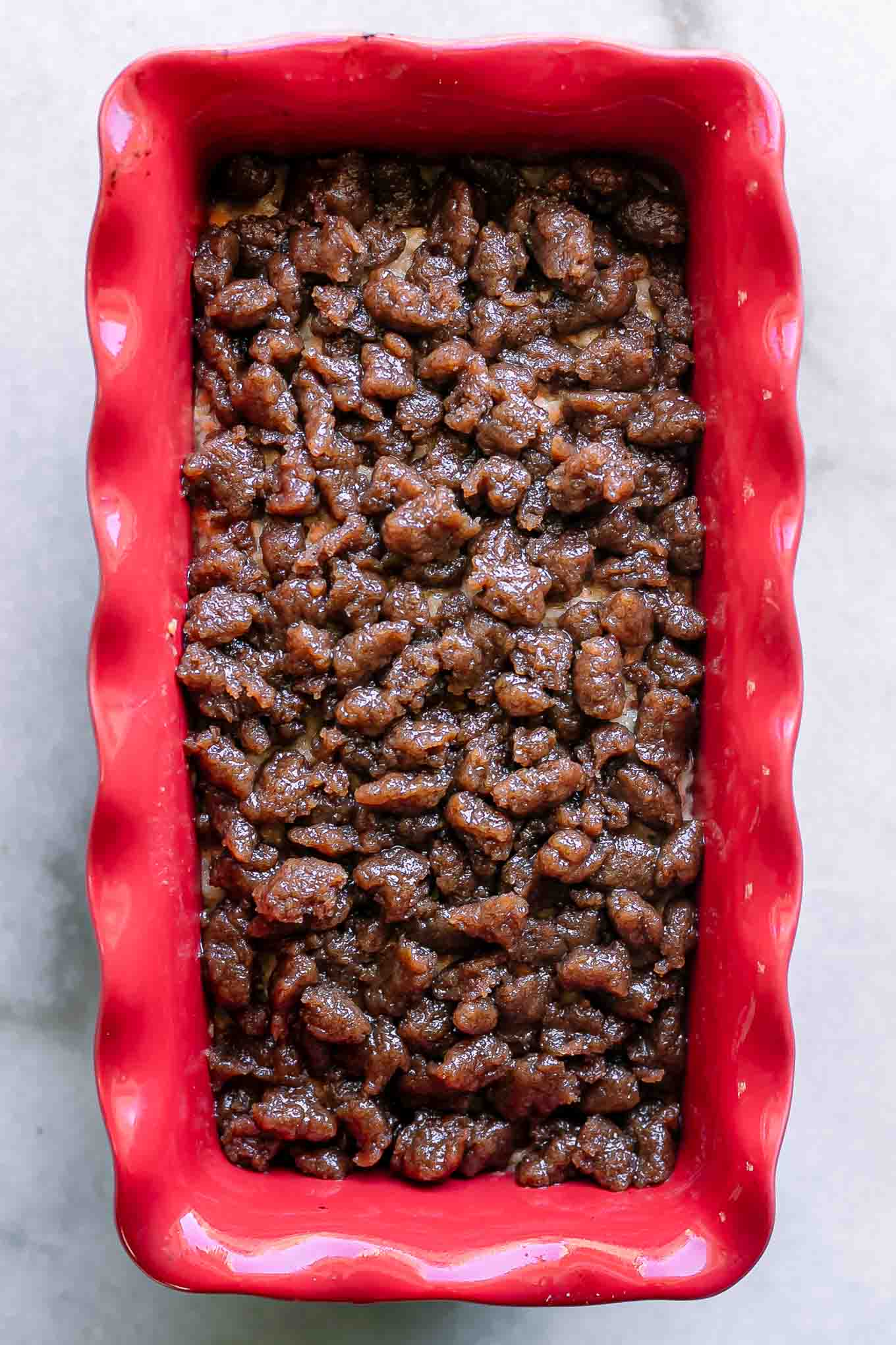 a red baking dish with bread batter and a sugar crumble on top before baking