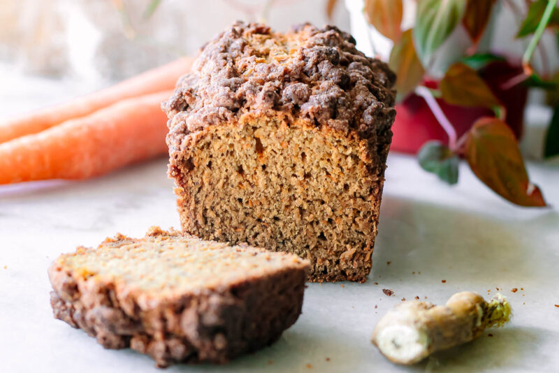 a sliced loaf of carrot cake bread on a table with fresh ginger and carrot
