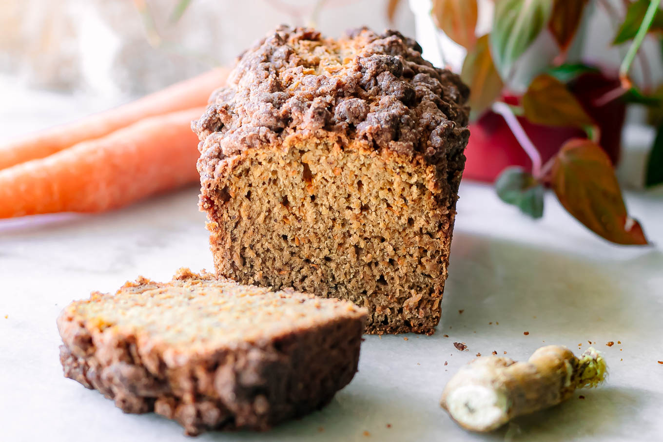 a sliced loaf of carrot cake bread on a table with fresh ginger and carrot