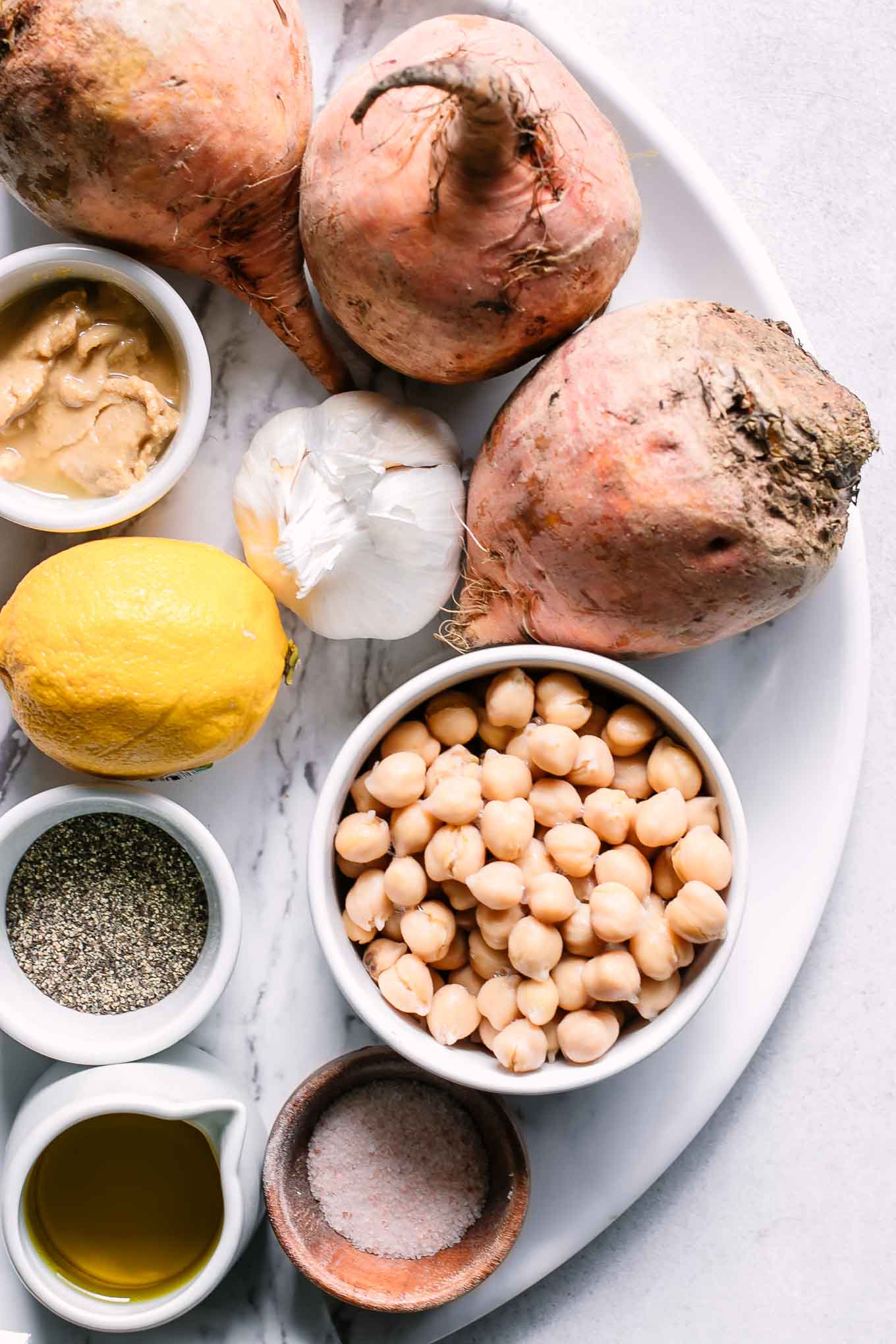 golden beets, garlic, lemons, and bowls of chickpeas, salt, pepper, oil, and tahini on a white table