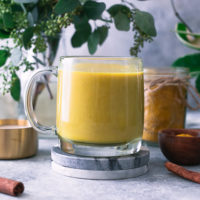 a yellow golden milk latte in a glass mug with cinnamon sticks