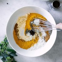 a hand mixing golden milk spices in a bowl with a whisk