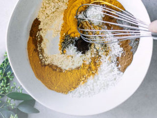 a white bowl with spices being mixed by a hand with a whisk and the words "homemade golden milk spice mix" in black and orange letters