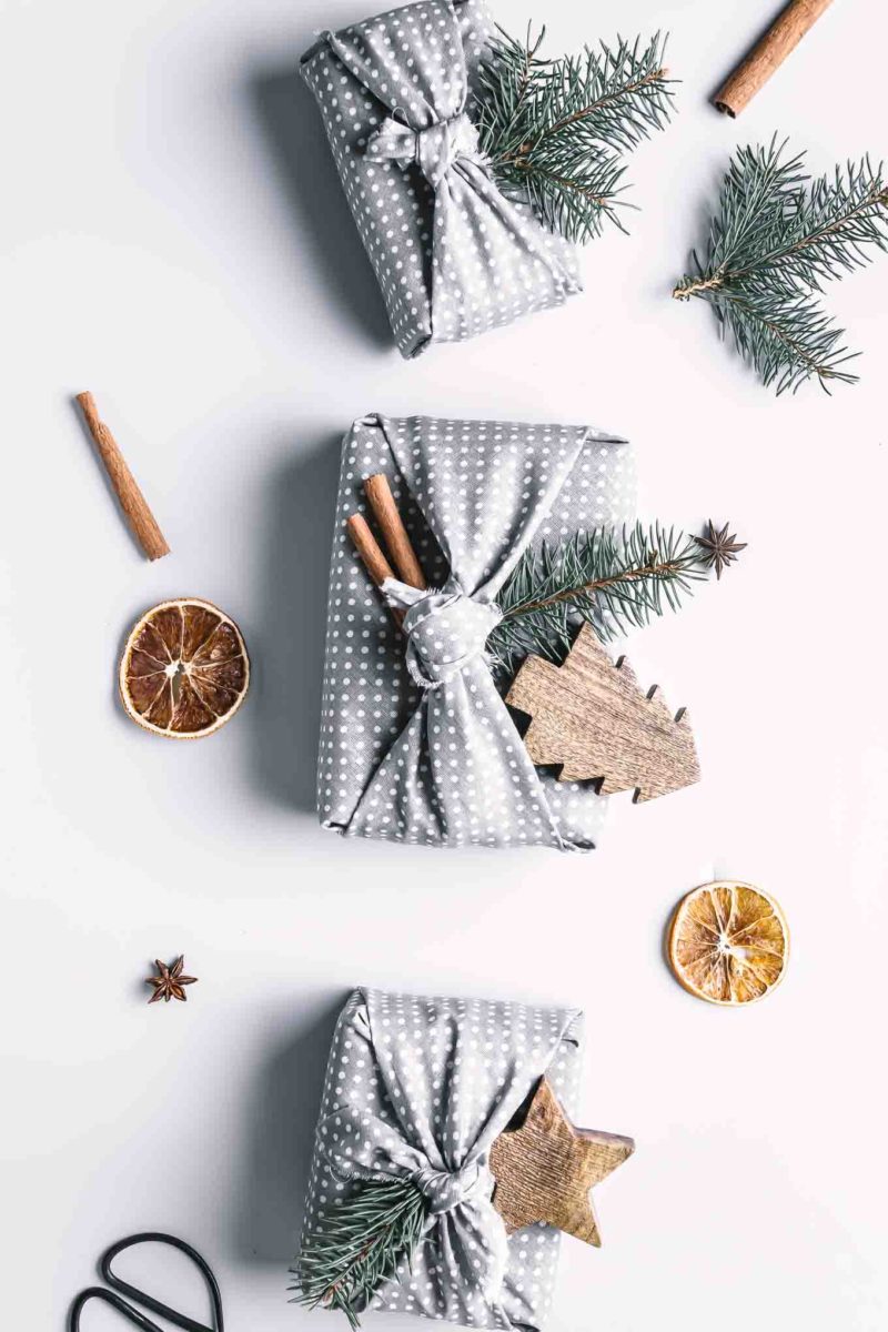 three gifts wrapped in reusable cloth wrapping paper on a white table with gift wrapping supplies