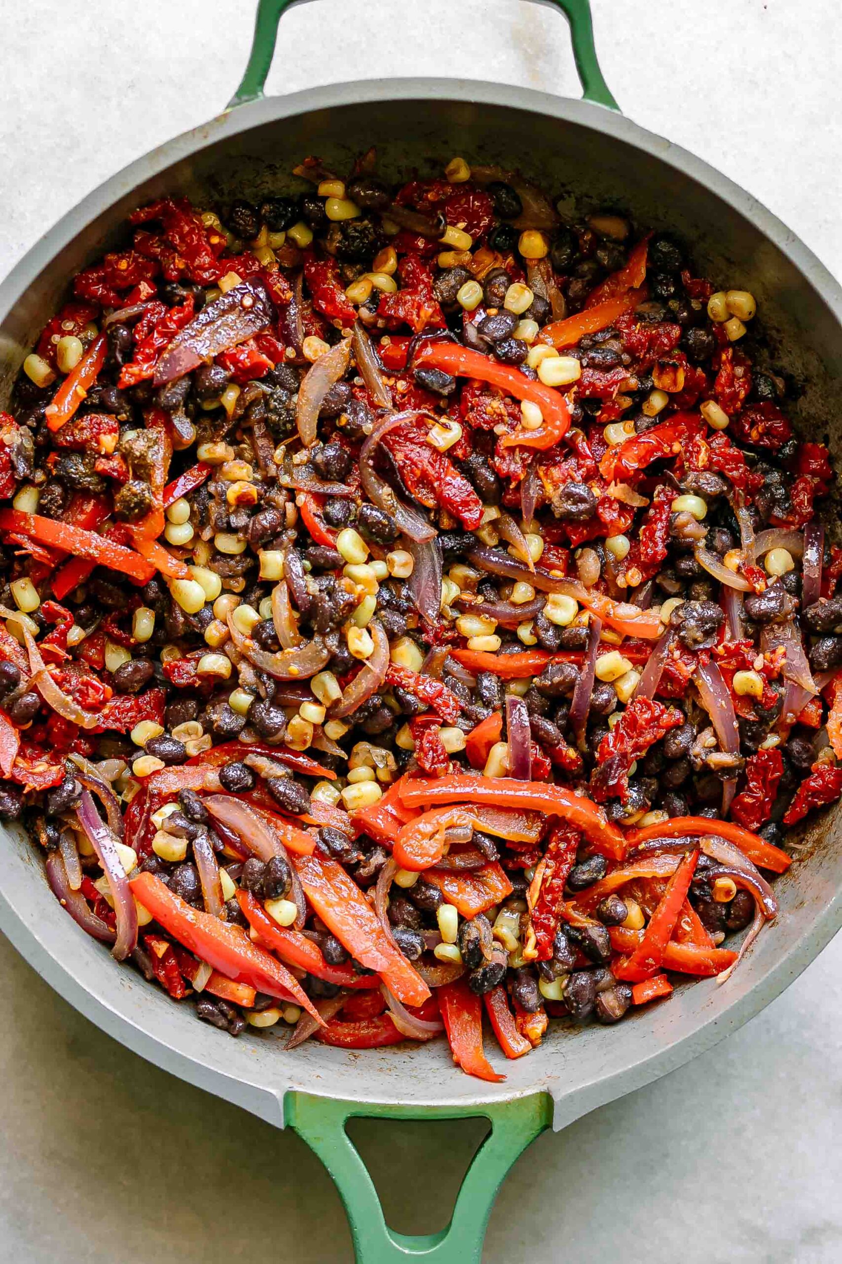 cooked bell peppers, onions, carrots, black beans, and sun-dried tomatoes in a pan
