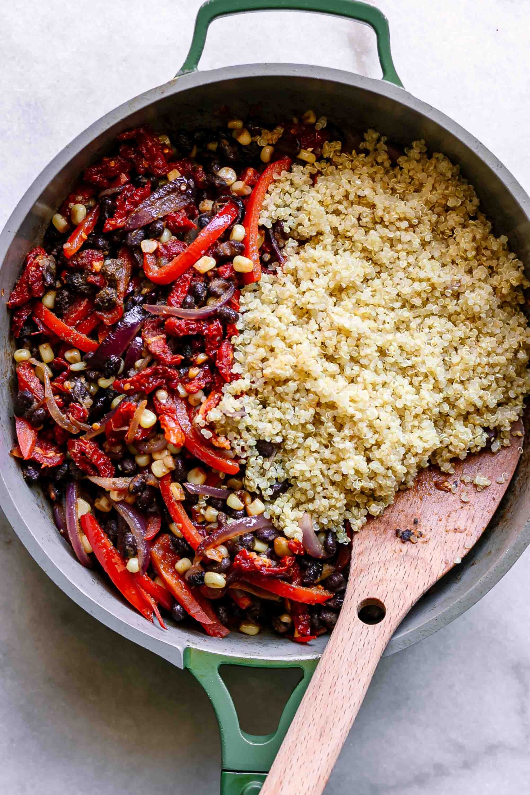 a pan with cooked quinoa and vegetables with a wooden spoon