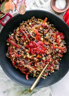 a quinoa bowl with black beans, bell peppers, and spicy harissa sauce on a white table