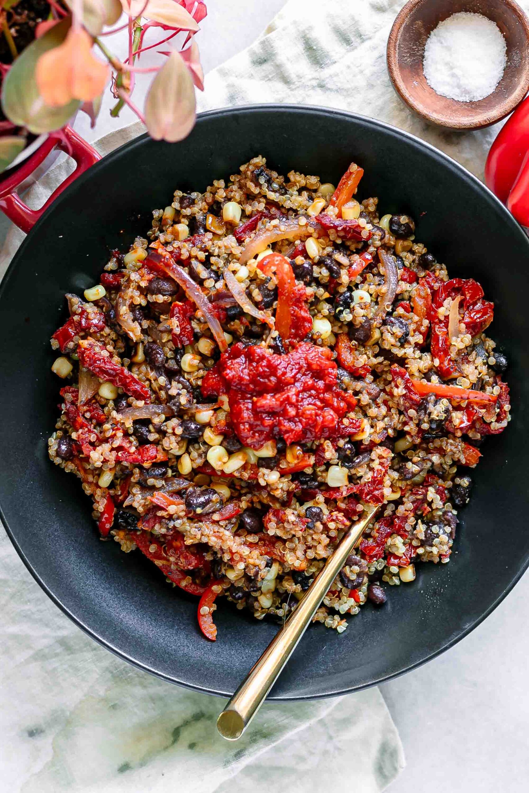 a quinoa bowl with black beans, bell peppers, and spicy harissa sauce on a white table