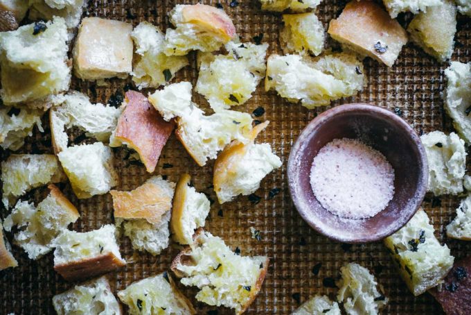 baked ciabatta croutons on a baking sheet with a bowl of salt
