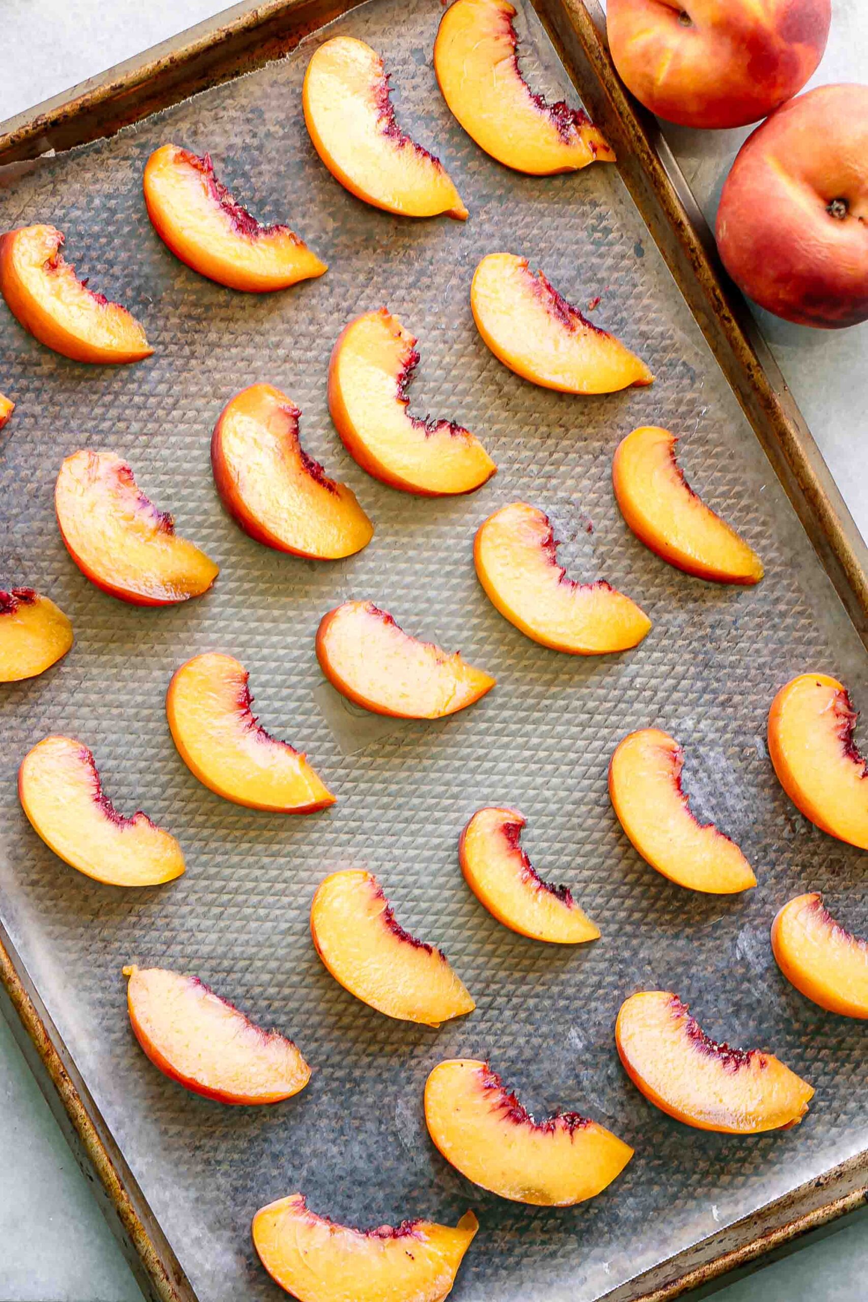 sliced peaches on a baking sheet covered in wax paper before freezing