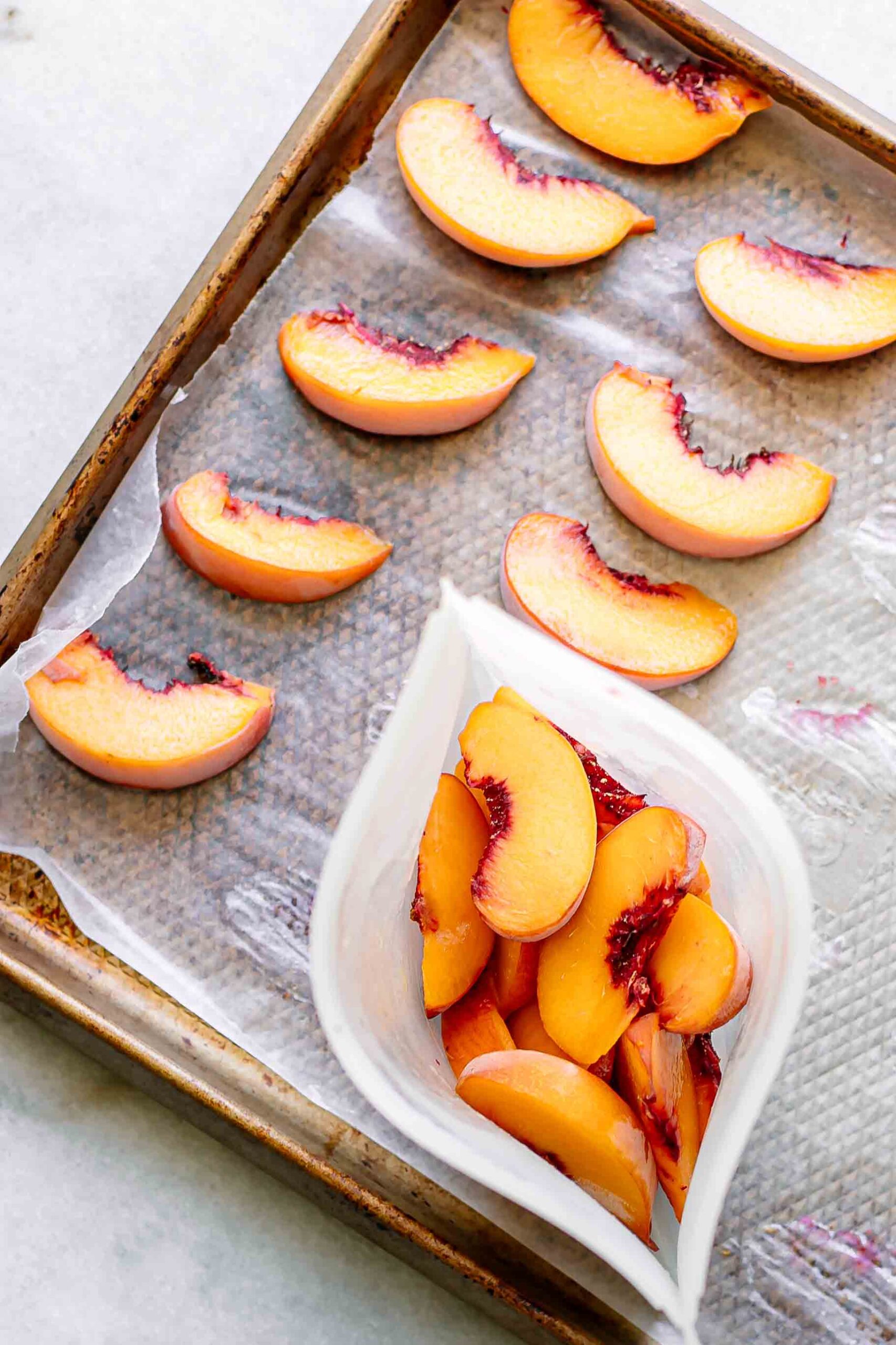 frozen peaches on a sheet pan after freezing and a silicone bag full of frozen peaches