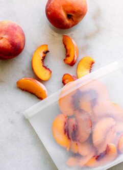 a freezer bag with frozen peaches on a white table with fresh peaches