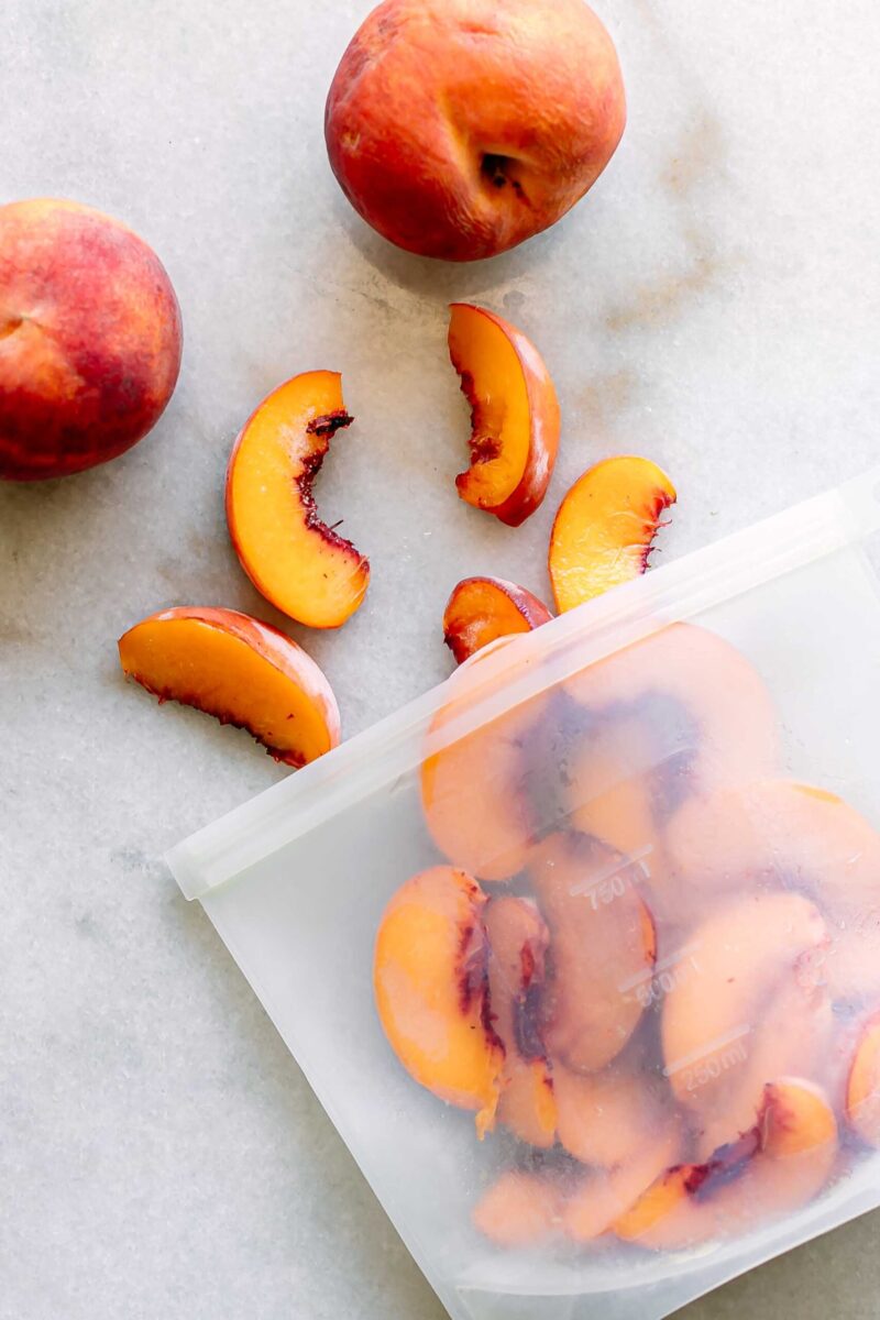 a freezer bag with frozen peaches on a white table with fresh peaches