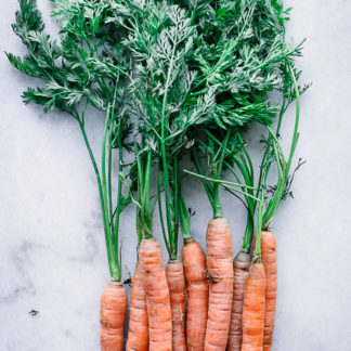 a bunch of orange carrots with green leaves on a white table