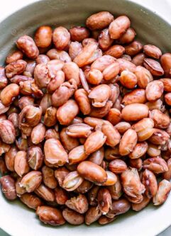 a bowl of cooked cranberry beans on a white table with bowls of spices and herbs