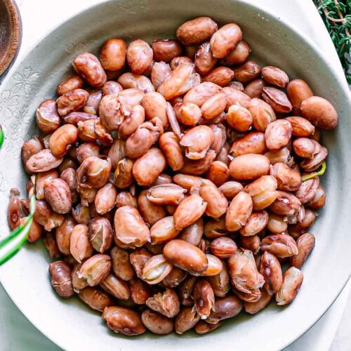 a bowl of cooked cranberry beans on a white table with bowls of spices and herbs