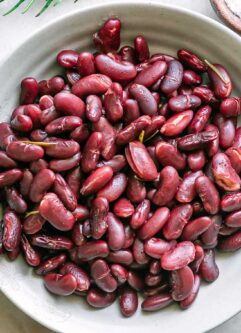 a bowl of cooked kidney beans on a white table with herbs and a bowl of salt