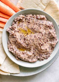 a bowl of kidney bean hummus on a plate with pita bread and carrot sticks