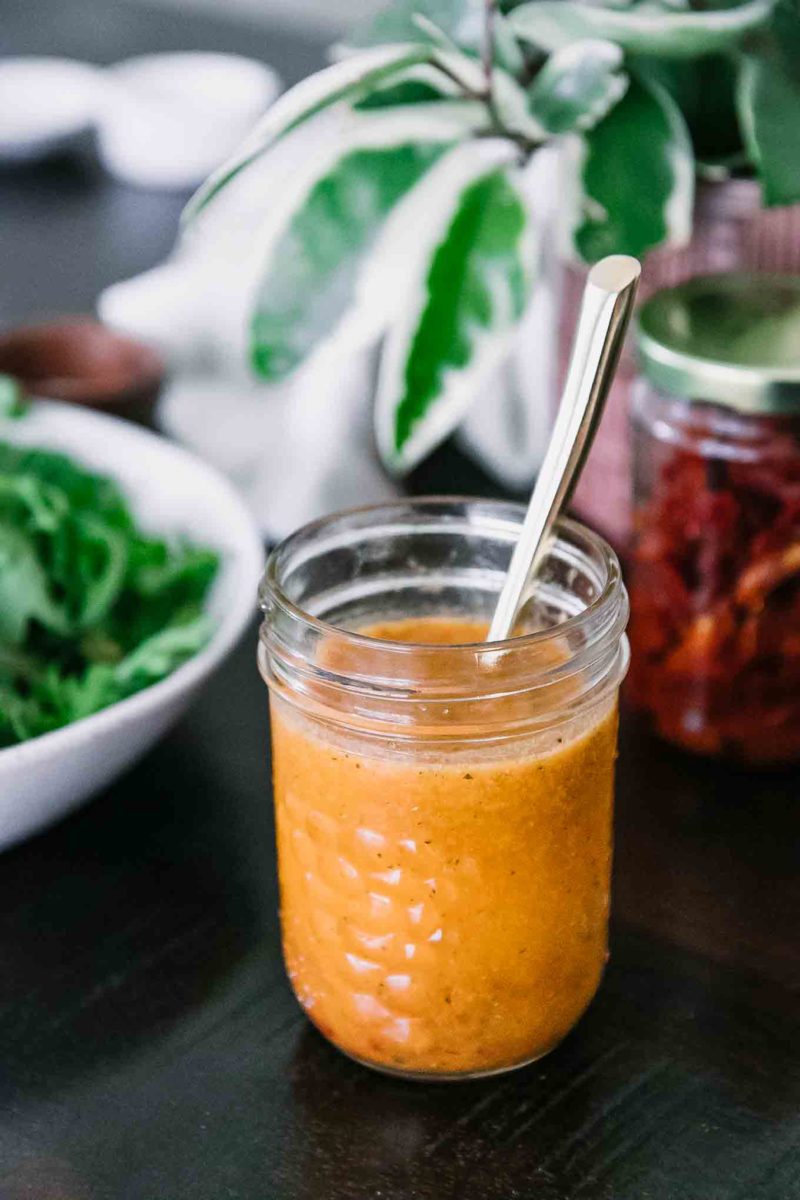 a mason jar with orange salad dressing and a gold spoon on a wooden table