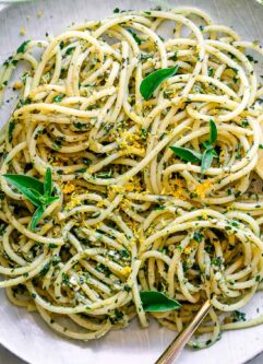 a white plate with lemon pesto pasta on a table with fresh lemons and fresh basil