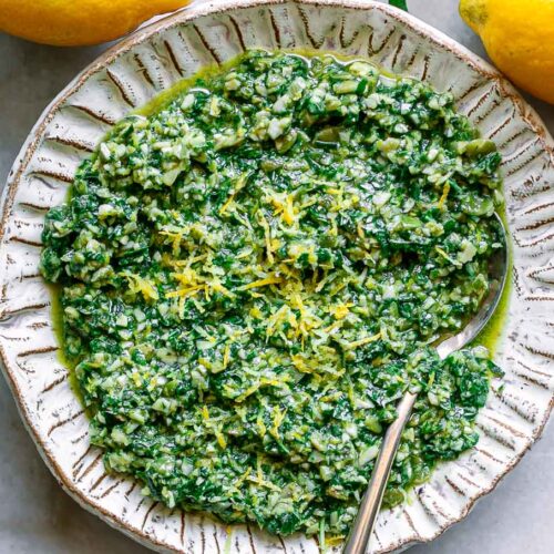 lemon pesto sauce with lemon zest as garnish in a white bowl with a gold fork on a white table