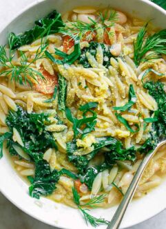 a bowl with lemon orzo soup with kale and lemon on a white table