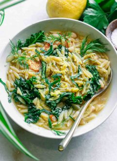 a bowl of lemon orzo white bean soup with kale in a white bowl with a gold fork