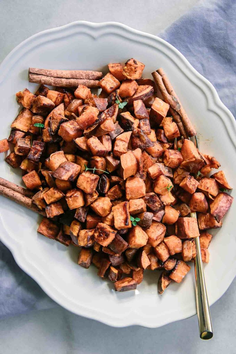 baked sweet potatoes on a white plate with cinnamon sticks