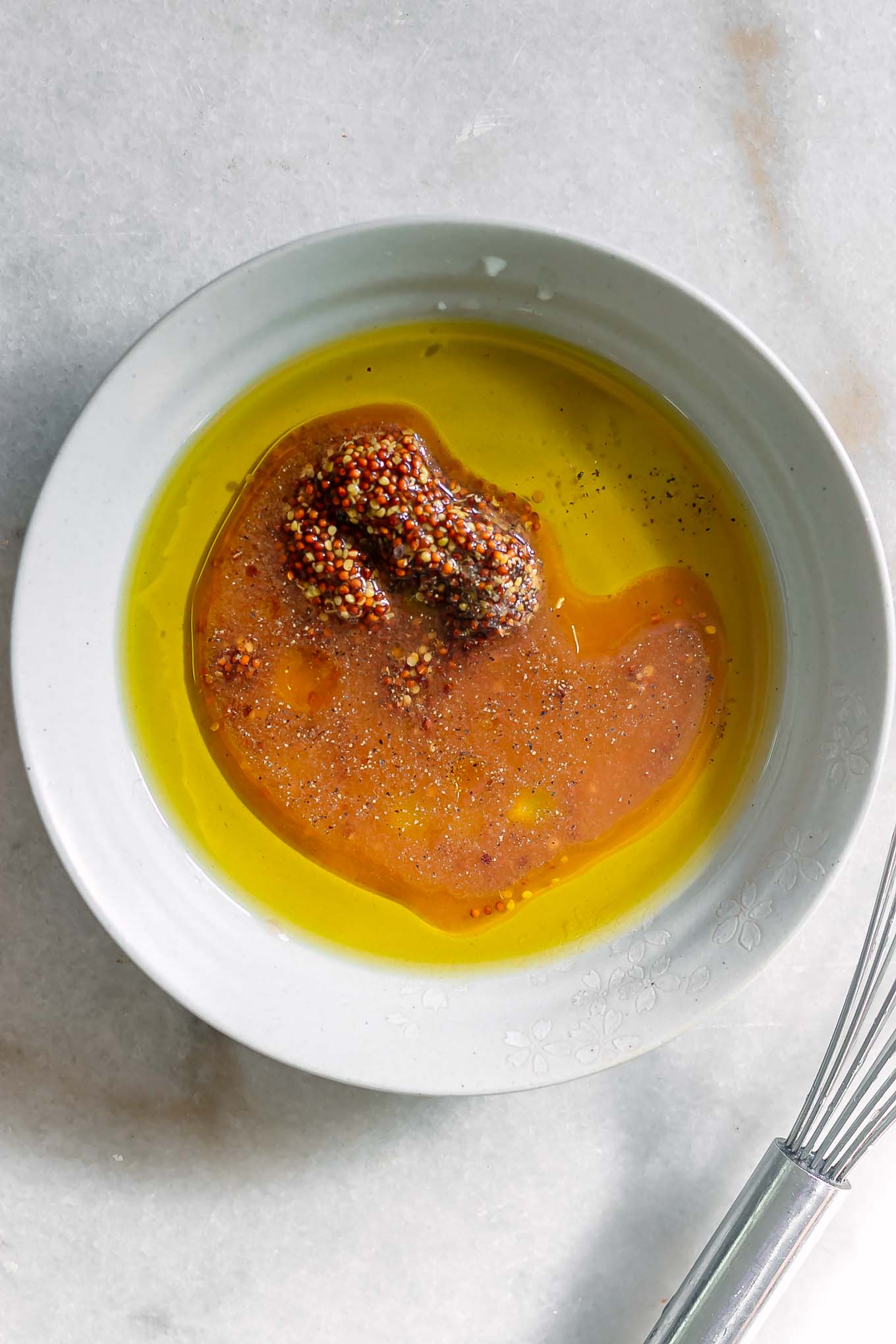 a bowl with olive oil, dijon mustard, maple syrup, vinegar, salt, and pepper on a white table