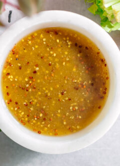 maple dijon salad dressing in a white bowl on a white table with vegetables