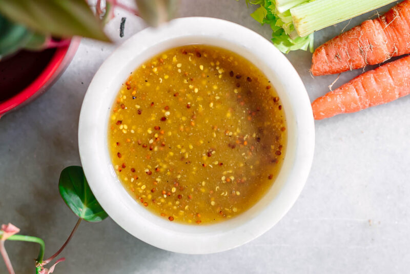 maple dijon salad dressing in a white bowl on a white table with vegetables