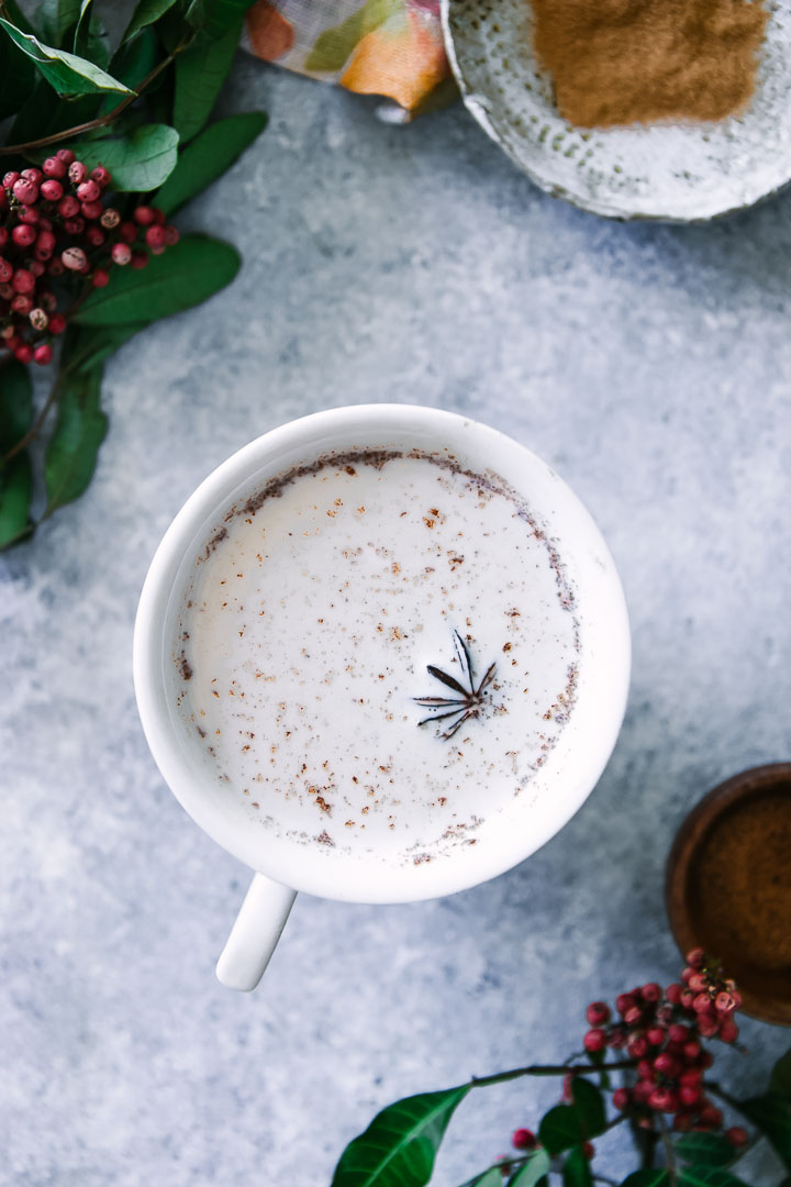 a chai latte in a white mug on a blue table with red flowers