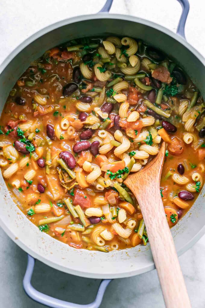 a pot of cooked minestrone soup on a white table with a wooden spoon