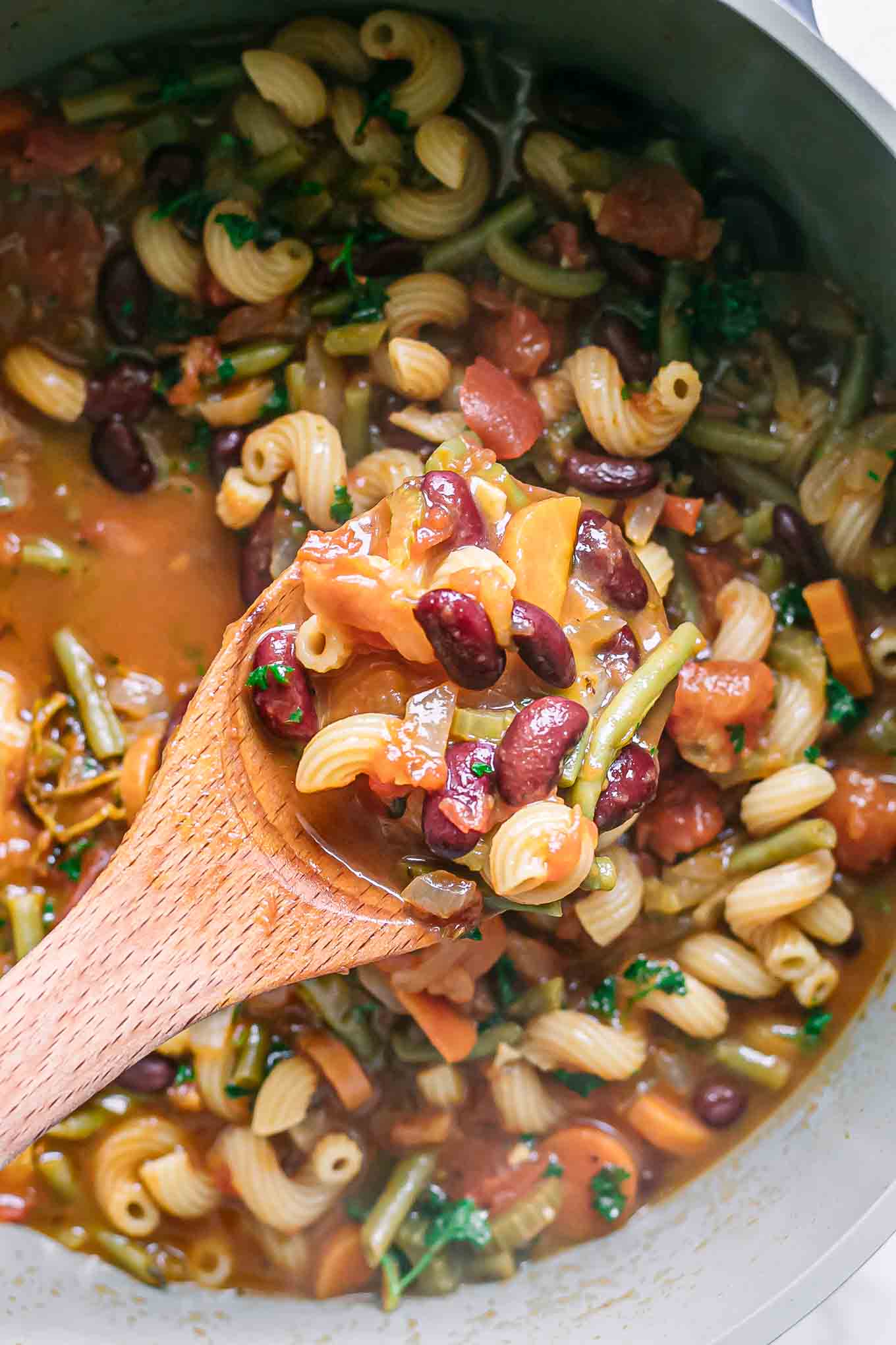 a wooden spoon with vegetables and beans above a pot of soup