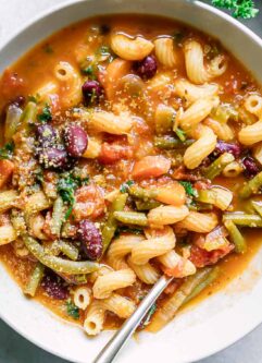 a white bowl of vegan minestrone soup on a white table with a gold fork