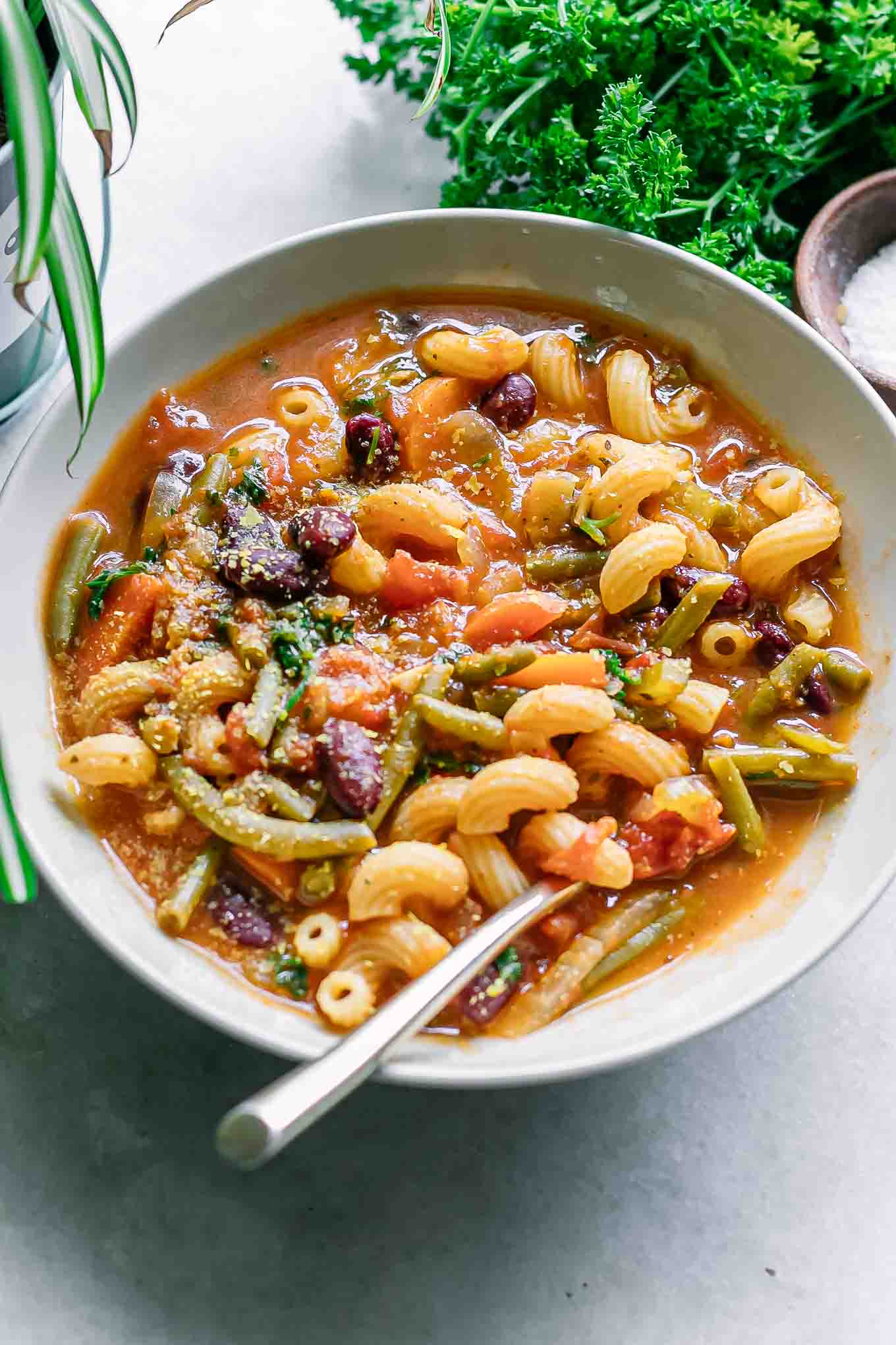 a bowl of plant-based minestrone soup with nutritional yeast on top in a white bowl on a white table
