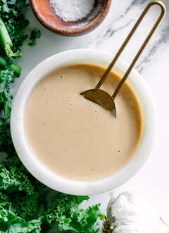 a white bowl with creamy miso tahini dressing with a gold spoon on a white table