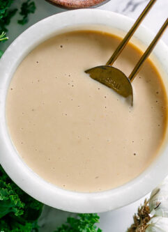 a miso tahini dressing in a white bowl on a white table with a gold spoon