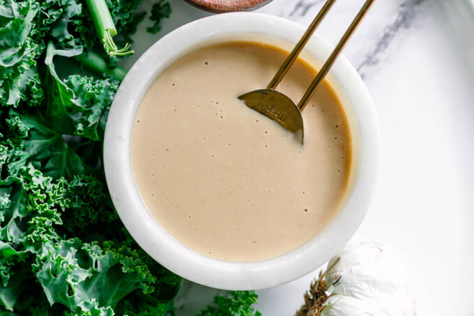 a miso tahini dressing in a white bowl on a white table with a gold spoon