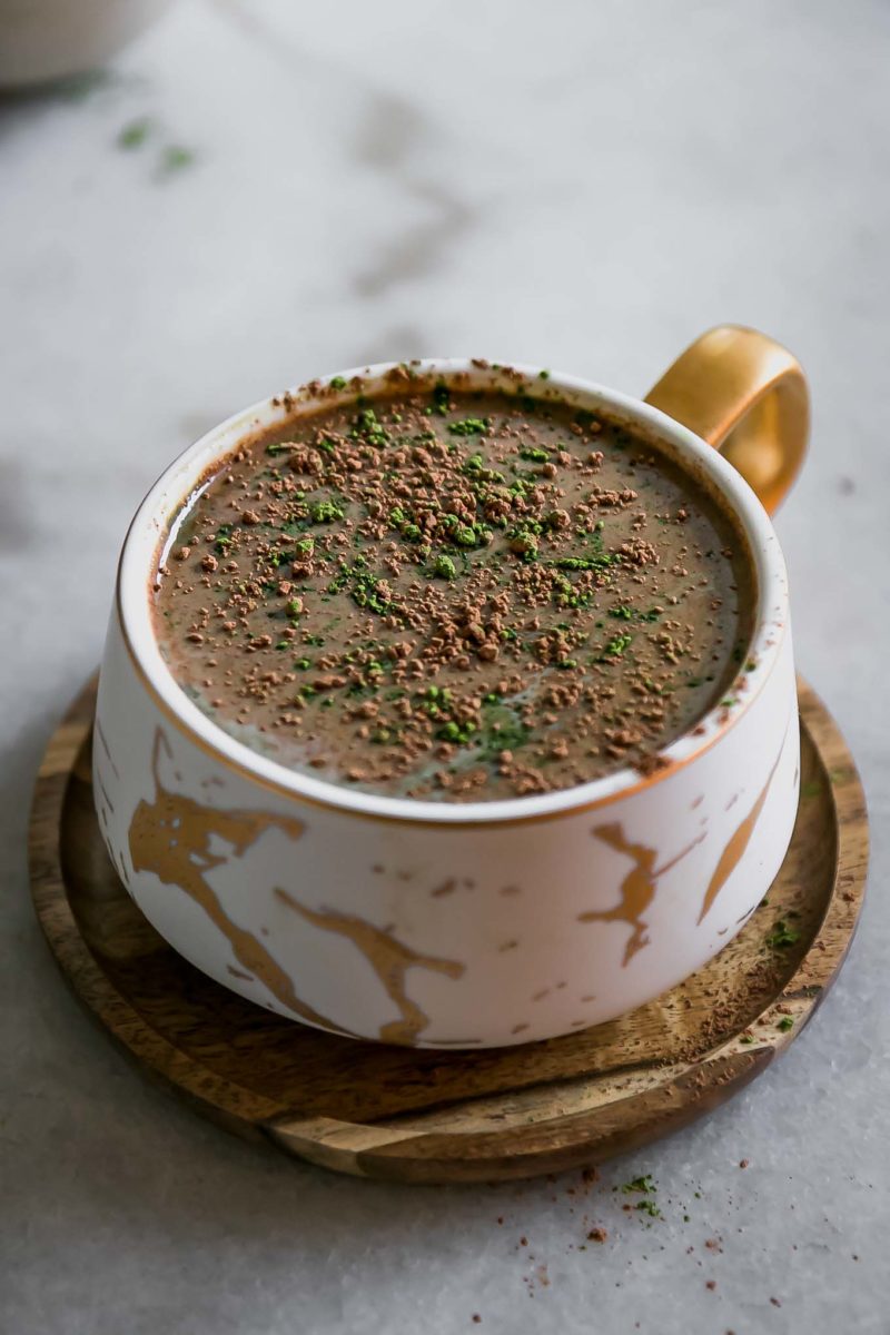 a matcha and mocha latte in a white ceramic mug on a wooden saucer on a white table